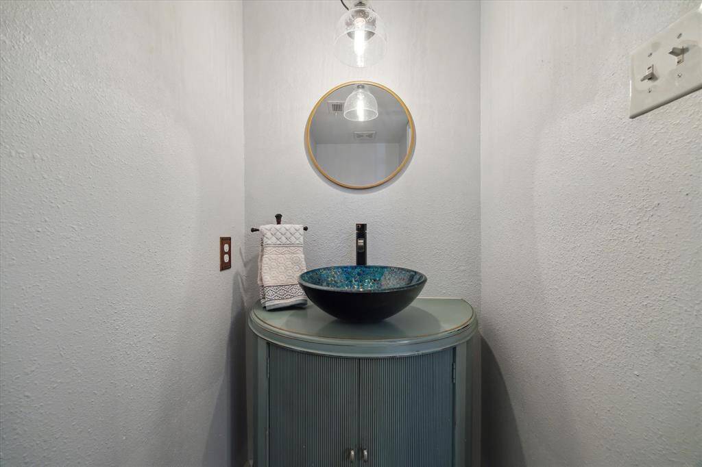 Remolded downstairs half-bath with a modern, artistic flair. Features a sleek round mirror, a unique vessel sink, and stylish lighting.