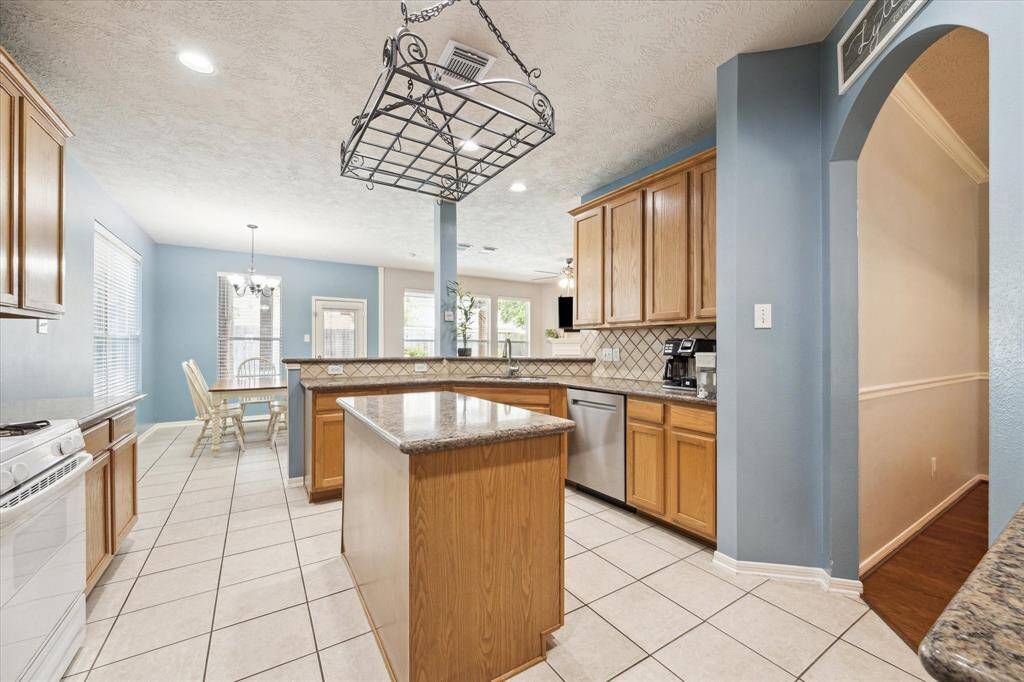 Bright kitchen with natural light, featuring tile flooring, wooden cabinetry, and a central island. The open layout flows into a cozy dining area, complemented by stylish backsplash.