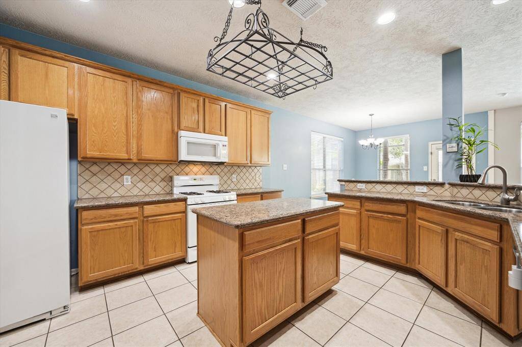This kitchen features warm wooden cabinetry, granite countertops, and a central island. and a spacious open layout with ample natural light from adjacent dining area windows.