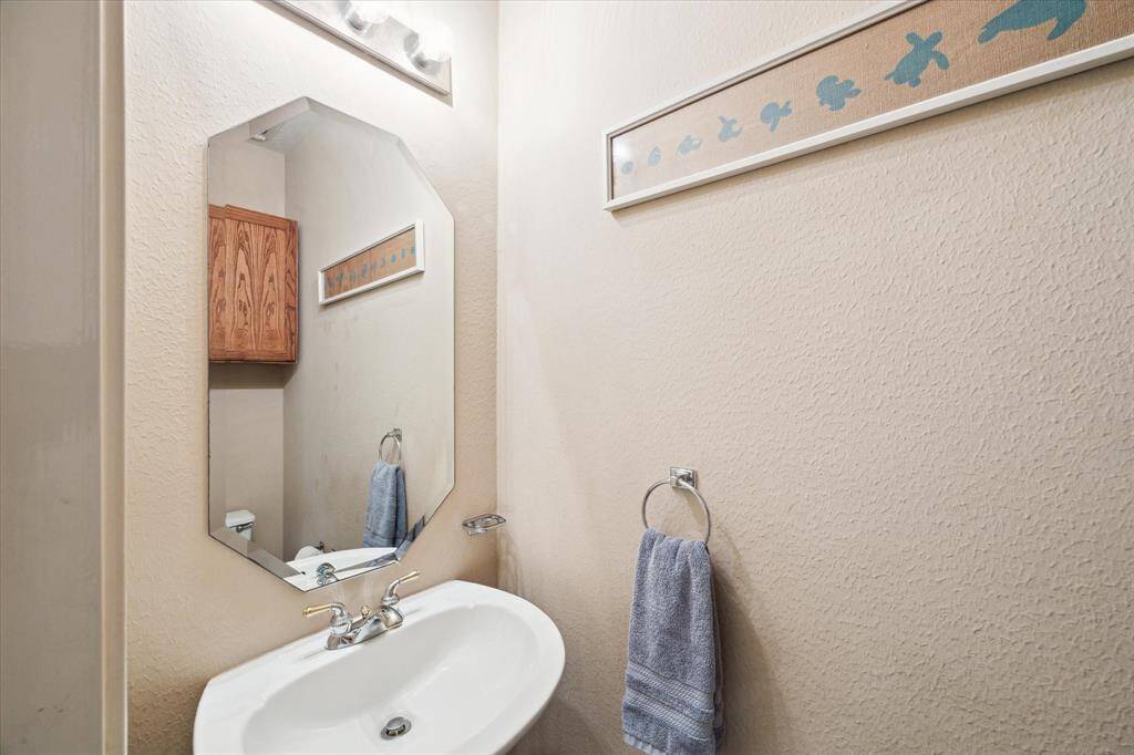 This photo showcases a half  bathroom with a modern sink, a decorative mirror, and a towel rack. The space features light-colored walls and a wooden cabinet for storage.
