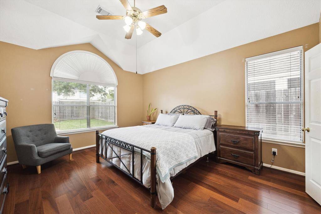 Bright primary bedroom with vaulted ceiling, large windows, and hardwood floors. Features a ceiling fan, and ample natural light.