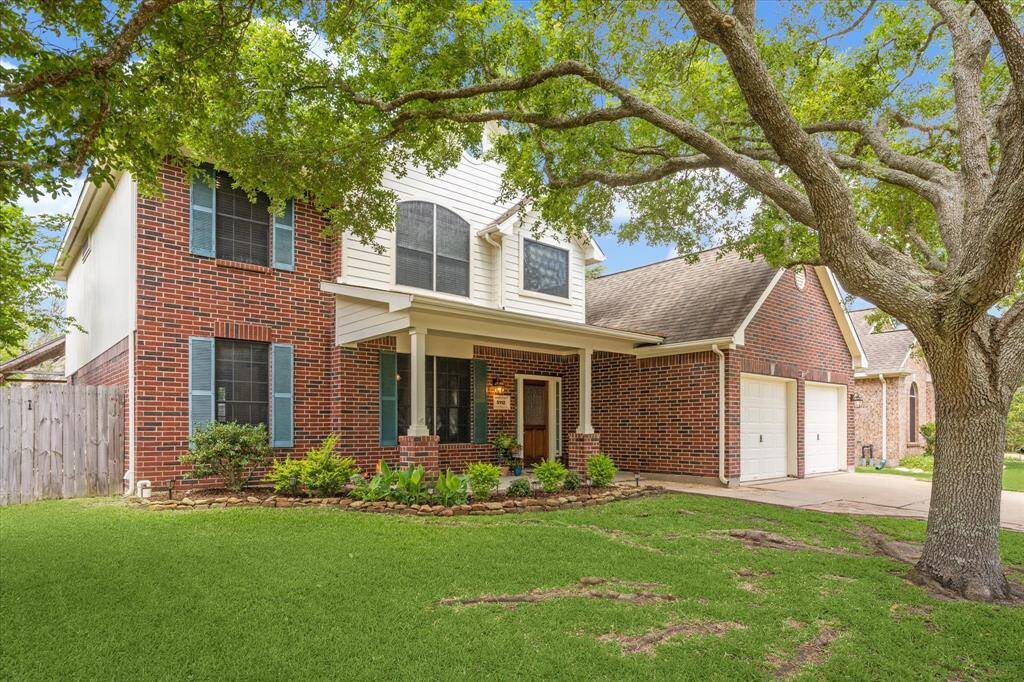 Charming two-story brick home with a welcoming front porch, double garage, and mature trees providing shade over a lush, green lawn. Ideal for family living.