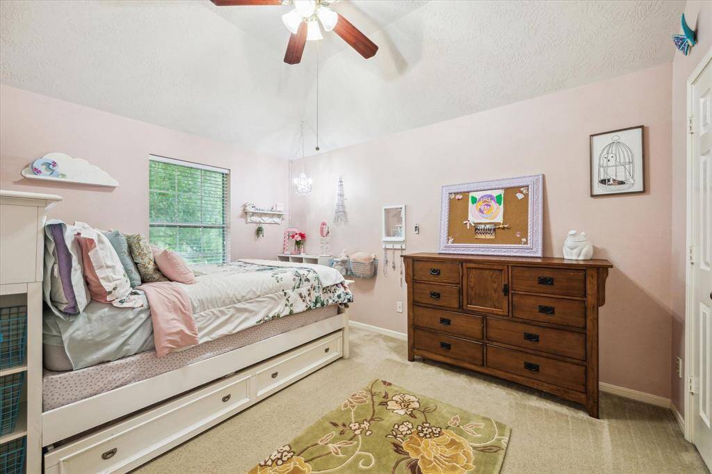 This bedroom features soft pink walls, a ceiling fan, and carpeting. A window providing natural light.