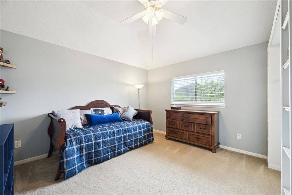 Cozy bedroom with neutral walls, ample natural light from a window. Carpeted floor and ceiling fan add comfort.