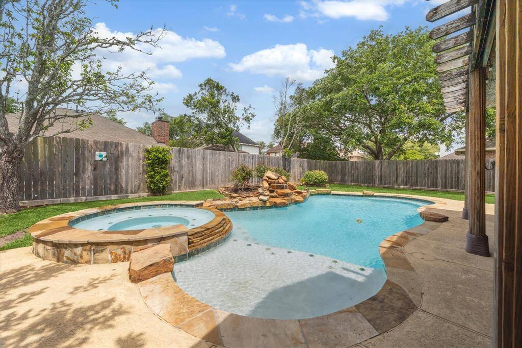 This backyard features a pool with a connected hot tub, surrounded by a wooden privacy fence and lush greenery, perfect for relaxation and entertaining.