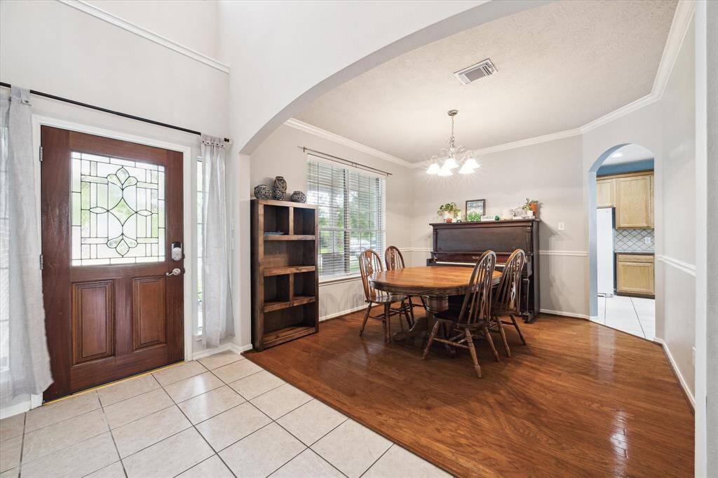 This photo showcases a bright dining area with hardwood flooring. The entryway has a decorative glass door and tiled flooring, seamlessly connecting to the kitchen through an arched doorway.