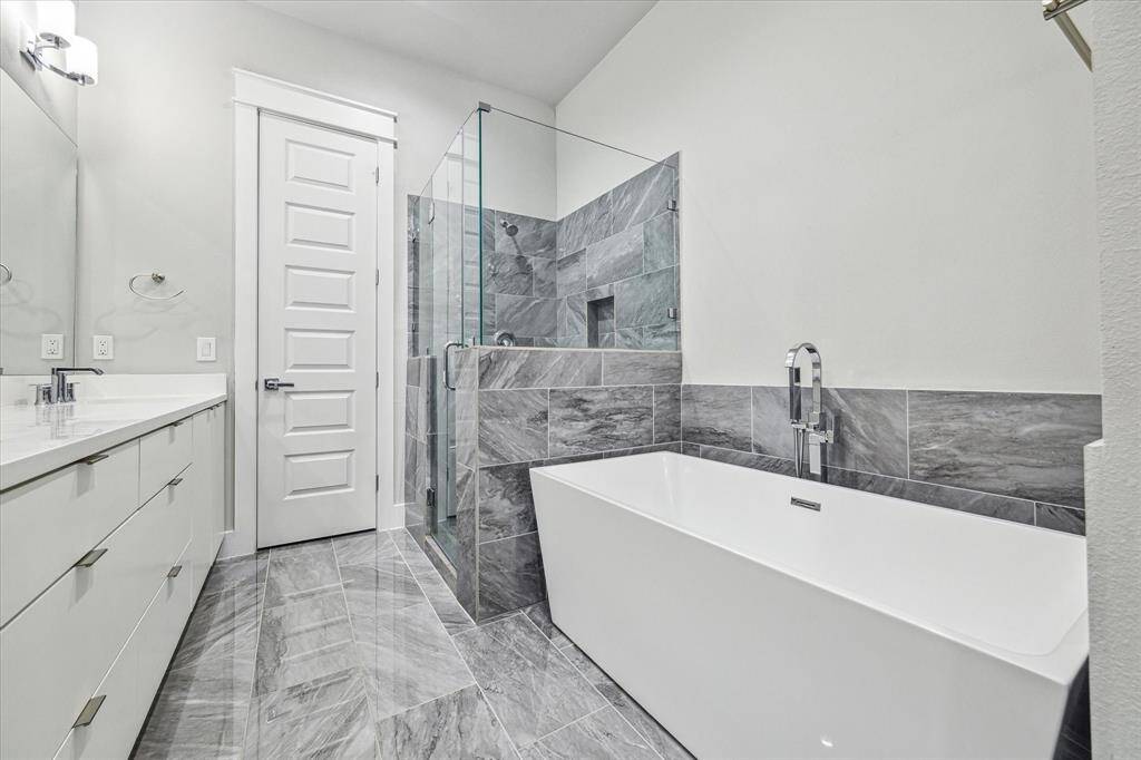 This modern bathroom features a sleek design with a spacious glass-enclosed shower, a freestanding bathtub, and elegant gray tile work. The room is bright and airy, with a double vanity providing ample storage.