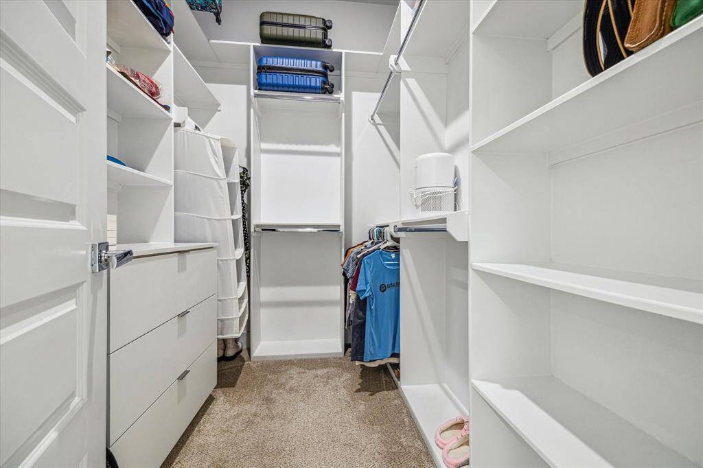 Spacious walk-in closet with ample shelving, hanging space, and built-in drawers, perfect for organized storage. Neutral colors and carpeted flooring enhance the cozy feel.