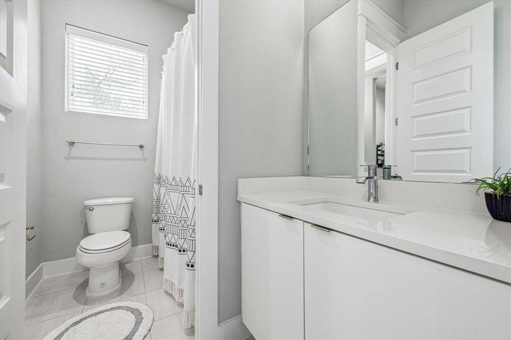 Modern bathroom with a sleek design featuring a white vanity, large mirror, and a shower with a geometric-patterned curtain. Natural light filters through a window, creating a bright and airy feel.