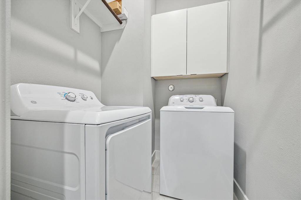 This photo shows a compact laundry room with a washer and dryer, overhead storage cabinets, and a neutral color scheme.