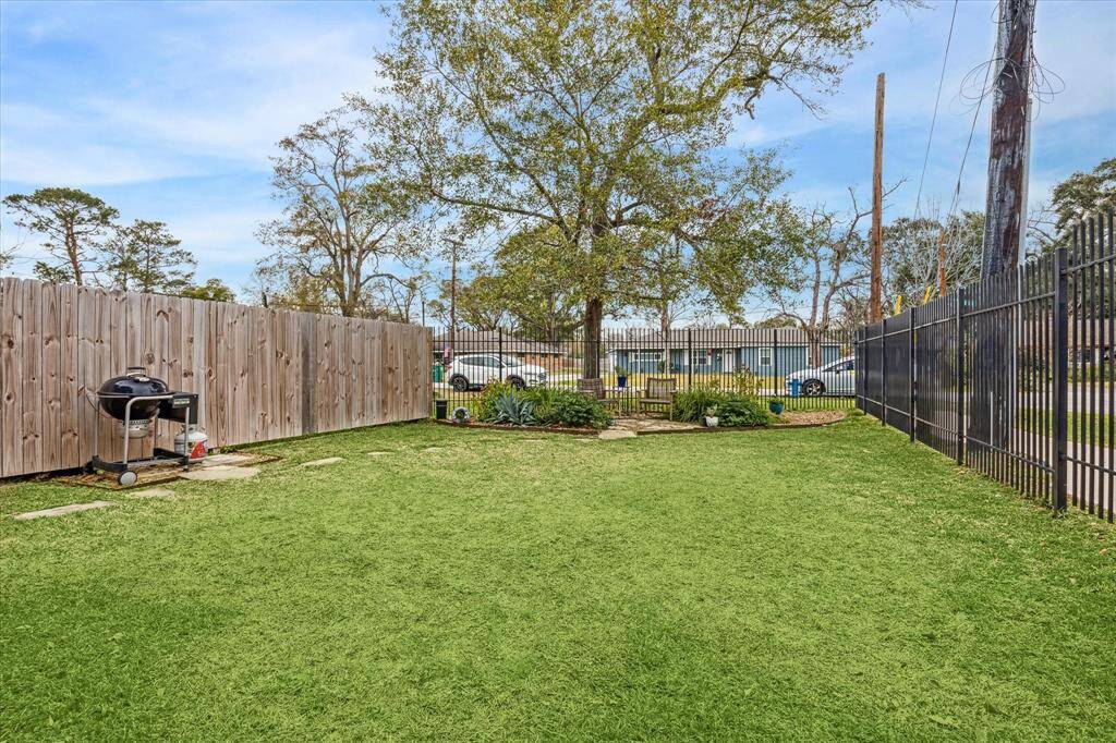 Spacious backyard with a lush lawn, bordered by a wooden fence and metal railing. Features a grill and a small garden area, offering a great space for outdoor activities.