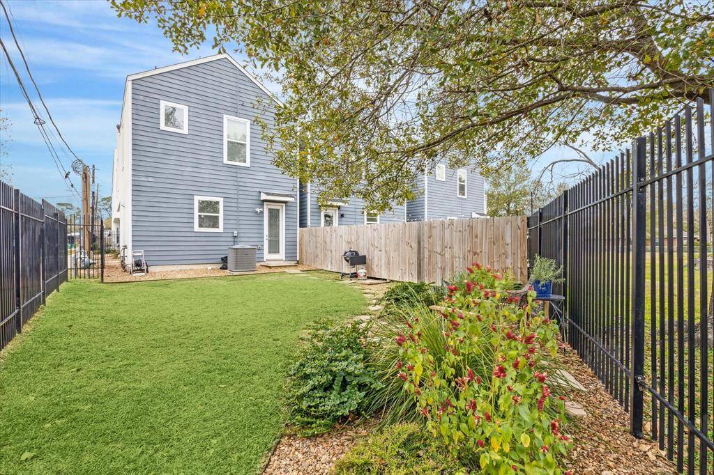 This photo features a modern, blue two-story home with a spacious fenced backyard. The yard includes a well-maintained lawn, a small garden with colorful flowers, and a patio area, perfect for outdoor activities and relaxation.