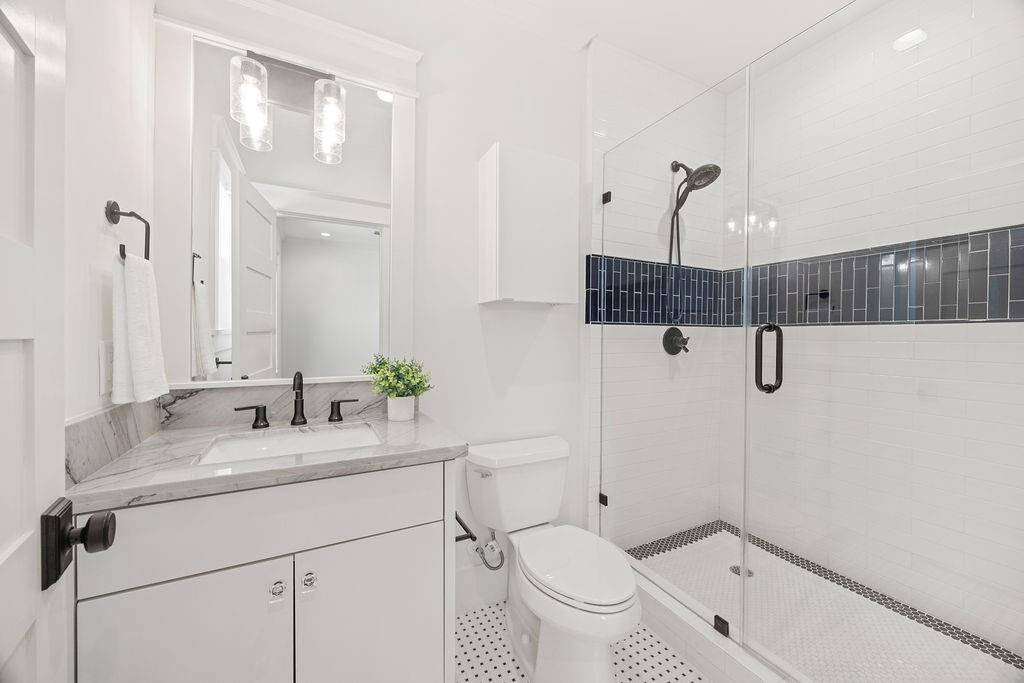 Crisp and modern en-suite bath with marble vanity, walk-in shower, and bold tile accent.