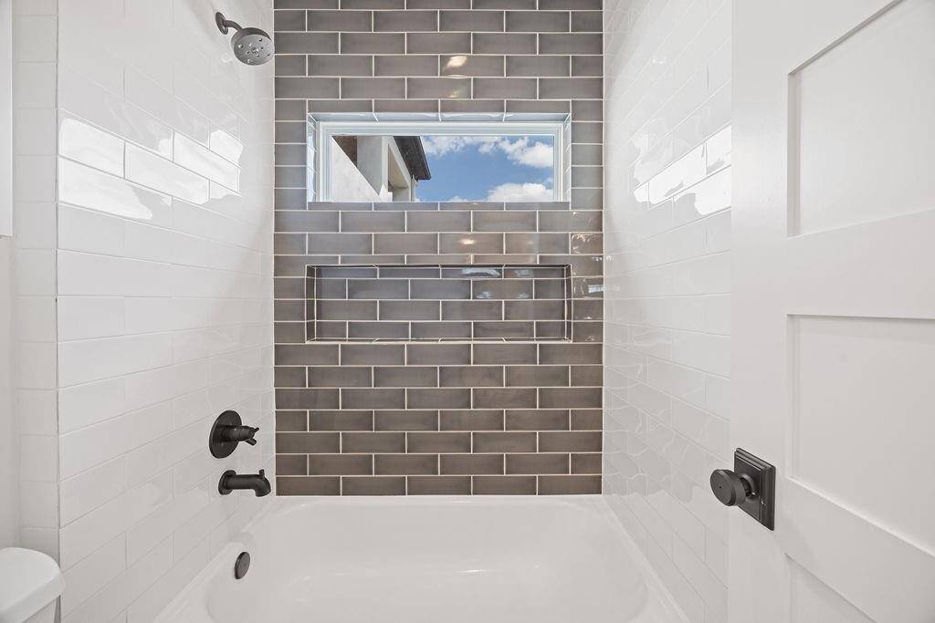 Striking tub/shower combo with contrasting tile, built-in niche, and a high transom window for natural light and privacy.