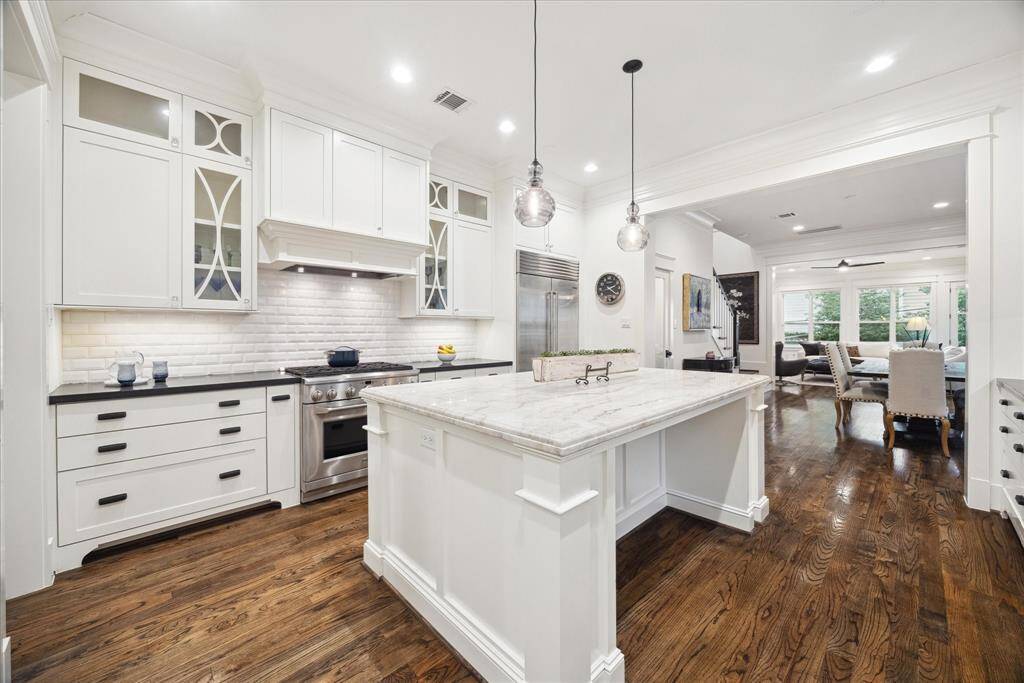 The kitchen seamlessly transitions into the living and dining spaces, highlighted by high ceilings, oak flooring, and abundant natural light—creating a warm and inviting atmosphere.