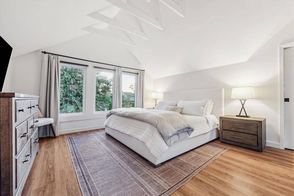 A picturesque primary suit equipped with custom walk-in closet, built-in storage and additional space perfect for an office nook, workout area, and more! Note beautiful foliage view and vaulted ceilings.