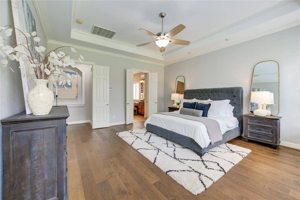 Serene primary suite with rich hardwood floors, custom molding, and oversized windows that flood the room with morning light
