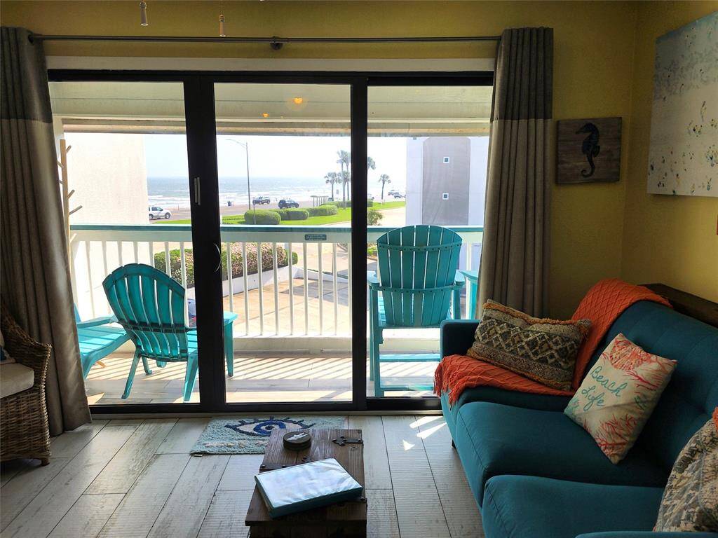 Bright living space with sliding glass doors leading to a balcony. Offers ocean views and features cozy seating with a beach-themed decor. Perfect for enjoying seaside relaxation.