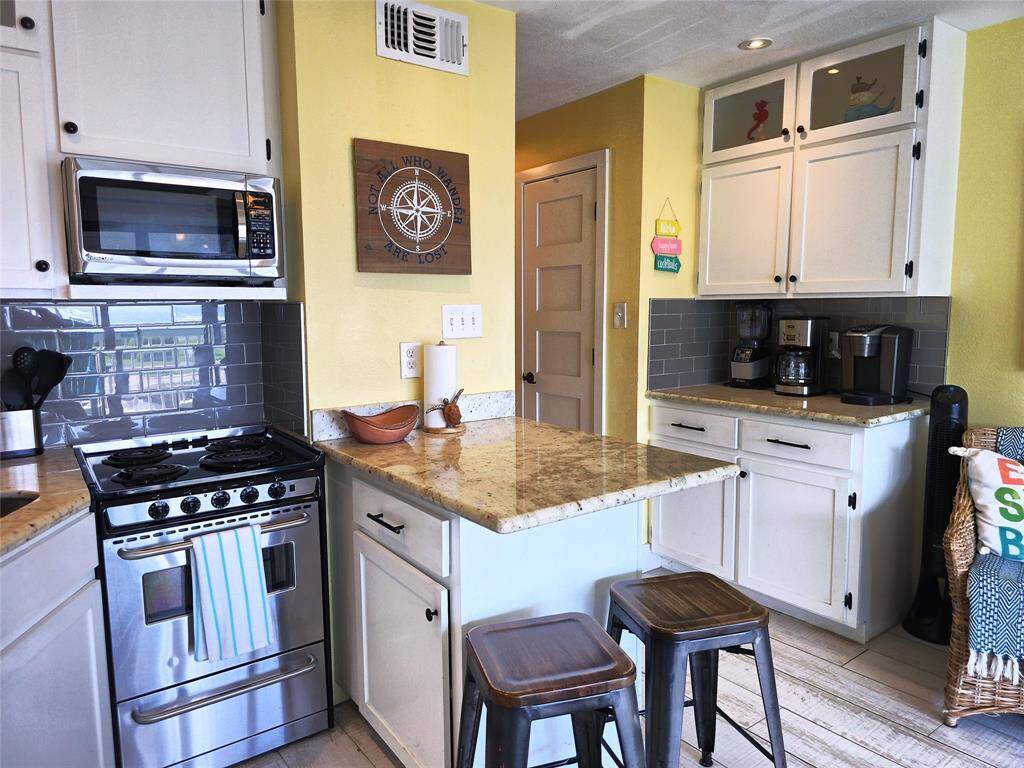 The kitchen features a simple layout with modern appliances, granite countertops, and stylish gray subway tile backsplash. It includes a small island with seating, white cabinetry for ample storage, and a warm yellow accent wall. Perfect for a functional and inviting cooking space.