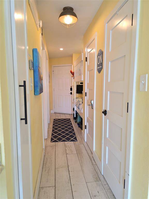 Bright and welcoming hallway with warm yellow walls, white doors, and light wood-look engineered flooring. Features recessed lighting and a stylish ceiling lamp, and carpet runner next to the built in bunk beds,  a comfortable place to sleep .