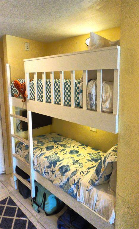 Built in bunk bed. The beds have colorful, patterned bedding, and there's a small ladder for access to the top bunk. The space underneath the lower bunk is used for storage, with bags neatly placed. Perfect for maximizing space in the units entryway.
