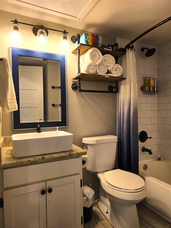 Bathroom features a modern design with a square vessel sink on a granite countertop, a stylish blue-framed mirror, and industrial-style lighting. The shower-tub combo has white subway tiles, and there's ample storage with wall-mounted shelves and a cabinet.