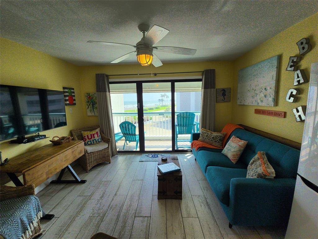 Bright and beachy living room with Gulf views, featuring a comfortable seating area, ceiling fan, and access to a balcony with outdoor seating. Decorated in shades of sun and water, it offers a relaxed coastal vibe.