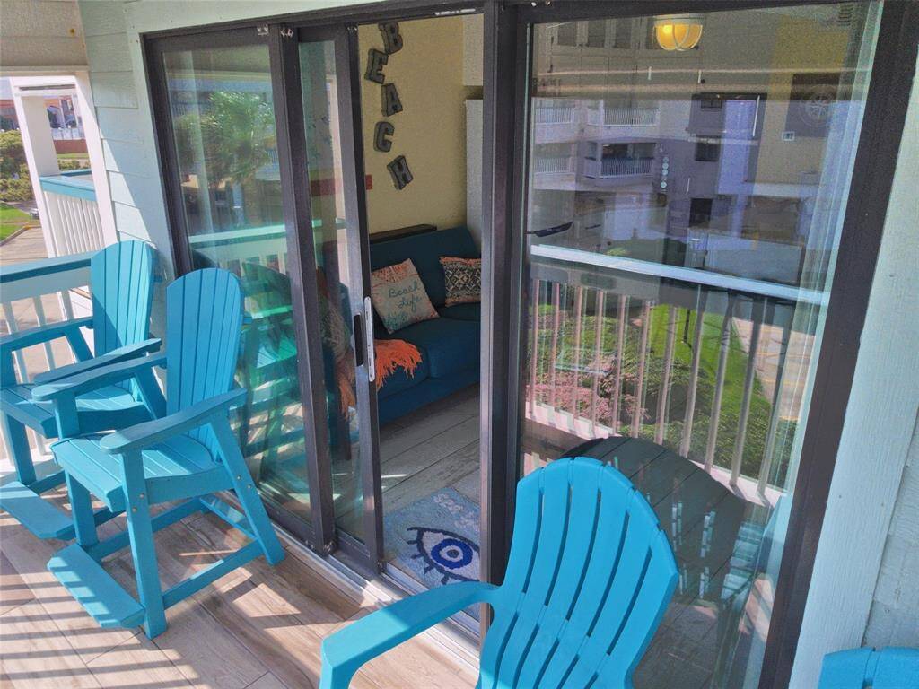 Balcony with bright blue Adirondack chairs and sliding glass doors leading into a living area. The space has a relaxing, beachy vibe, perfect for enjoying the outdoors.