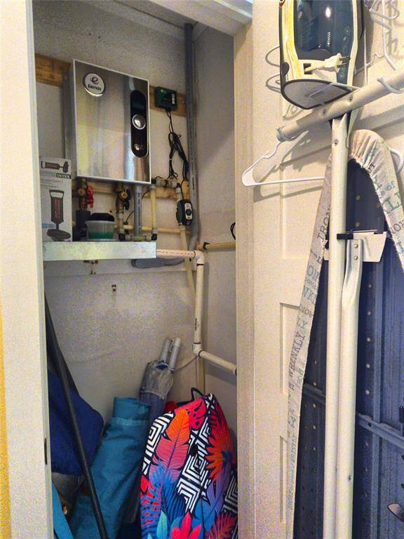 Utility closet featuring a tankless water heater and plumbing lines. It includes storage space for cleaning supplies, an ironing board, and an iron. Ideal for efficient use of space in a home.