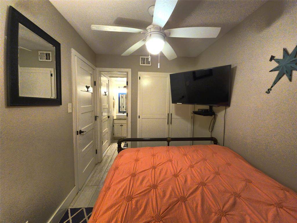 Cozy bedroom featuring a ceiling fan, mounted TV, and a bright orange bedspread. The room includes a mirror and has access to an adjoining bathroom through a door. The space is compact and functional, ideal for comfort and relaxation.
