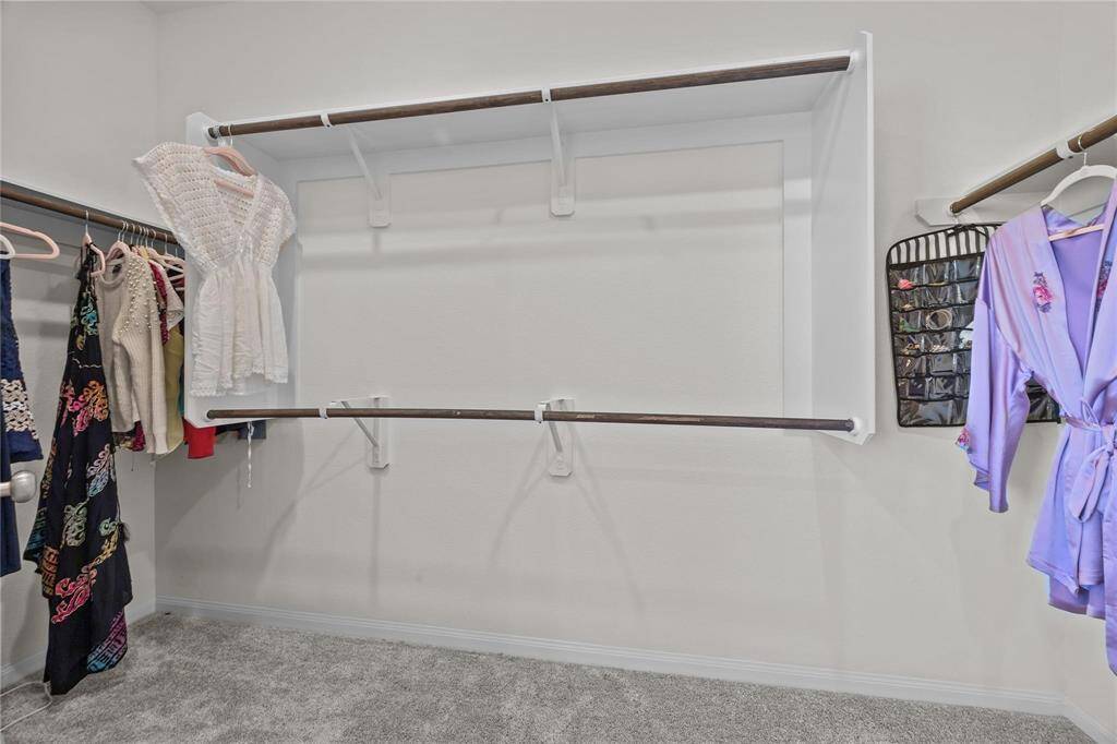 This photo shows a spacious walk-in closet with multiple hanging rods and shelves (not shown), offering ample storage and organization for clothing. The neutral color palette and carpeted floor add a cozy touch.
