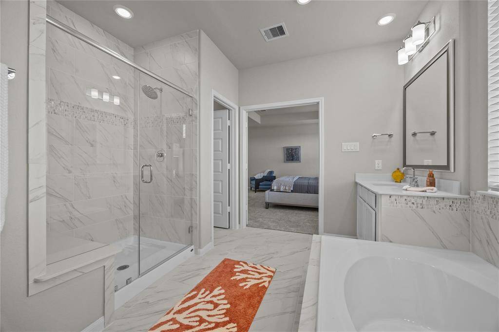 This bathroom features a luxurious design with a spacious tub, dual vanities, and modern lighting. A large window provides natural light, and there's a walk-in shower. Ample closet space is accessible from the bathroom, enhancing convenience.