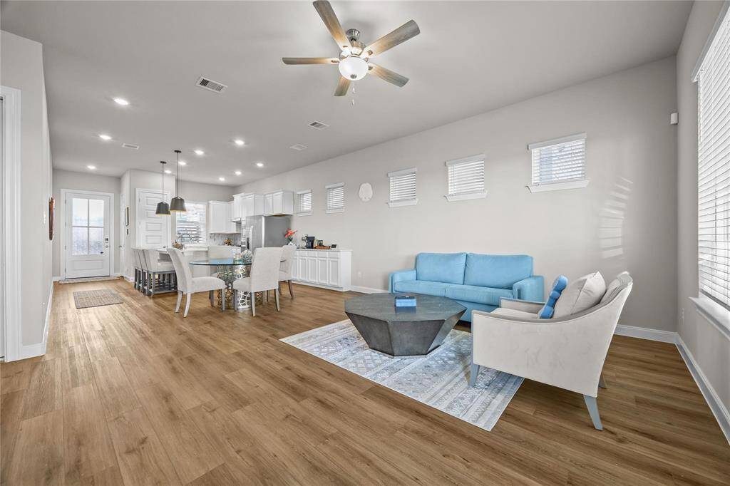 Open-concept living area with neutral paint and wood-tone vinyl plank flooring. It features a cozy seating area breakfast area, and a great space for a coffee bar with storage underneath. A ceiling fan adds comfort and the staircase leads to the upper level.