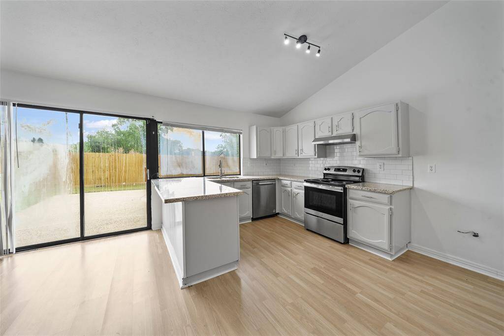 Bright, open kitchen with modern appliances, white cabinets, and granite countertops. It features a spacious layout with light wood flooring and large sliding doors leading to the backyard, offering plenty of natural light.