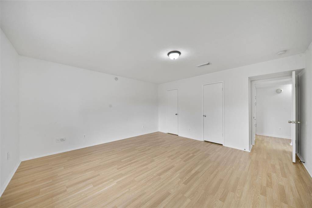 Spacious main bedroom with light wood flooring, white walls, and a central ceiling light.