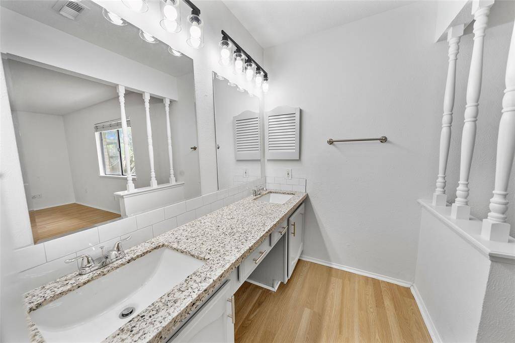 This main bedroom features a spacious dual-sink vanity with granite countertops, abundant lighting, and a large mirror.