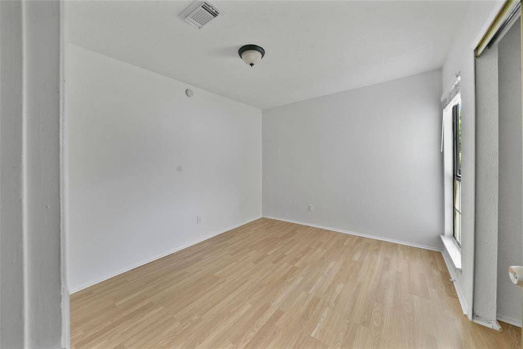 This secondary bedroom features clean, white walls and light wood flooring, creating a bright and open space. A large window allows for natural light, and there's a ceiling light fixture for additional illumination.