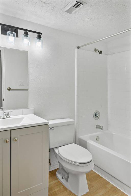 This bathroom features a clean, modern design with a white bathtub-shower combo, a single vanity with storage, and a sleek light fixture above a large mirror. The wood-style flooring adds warmth to the space.