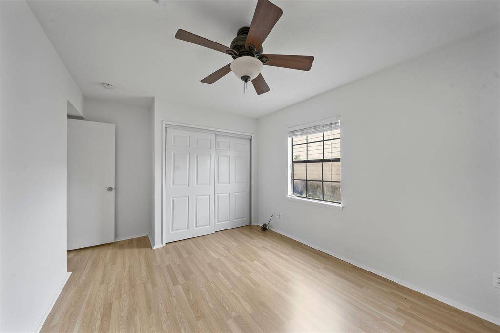 Bright, airy bedroom with light wood floors, a ceiling fan, and a window for natural light. It features a closet with sliding doors and a simple, clean design.