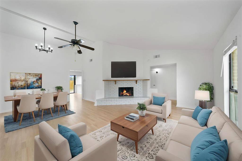 Virtually staged - Spacious, open-concept living and dining area with a high ceiling and a ceiling fan. The room features a cozy brick fireplace and large windows that let in plenty of natural light. e.