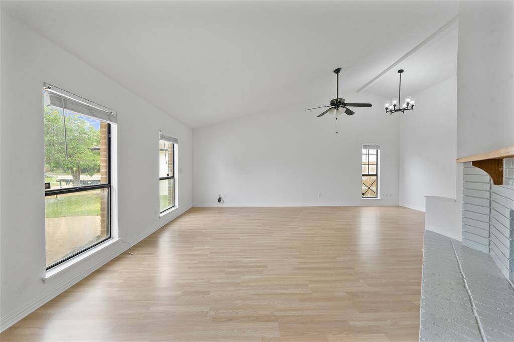 This spacious living area features light wood flooring, high ceilings, large windows for natural light, and a ceiling fan. The room is open and airy, providing a versatile space for relaxation or entertaining.