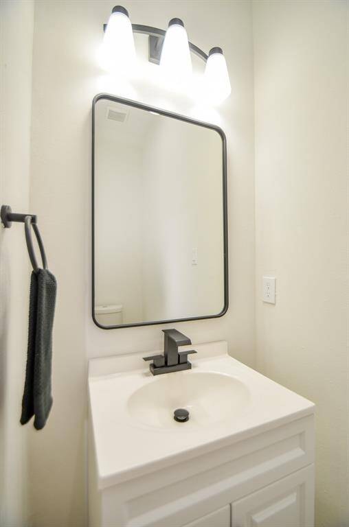 This bathroom features a modern vanity with a sleek black faucet and a rectangular mirror. It is well-lit with a three-light fixture, offering a clean and minimalist design. Just off of entry, this the guest bathroom, located near the entryway, adjacent to the garage.