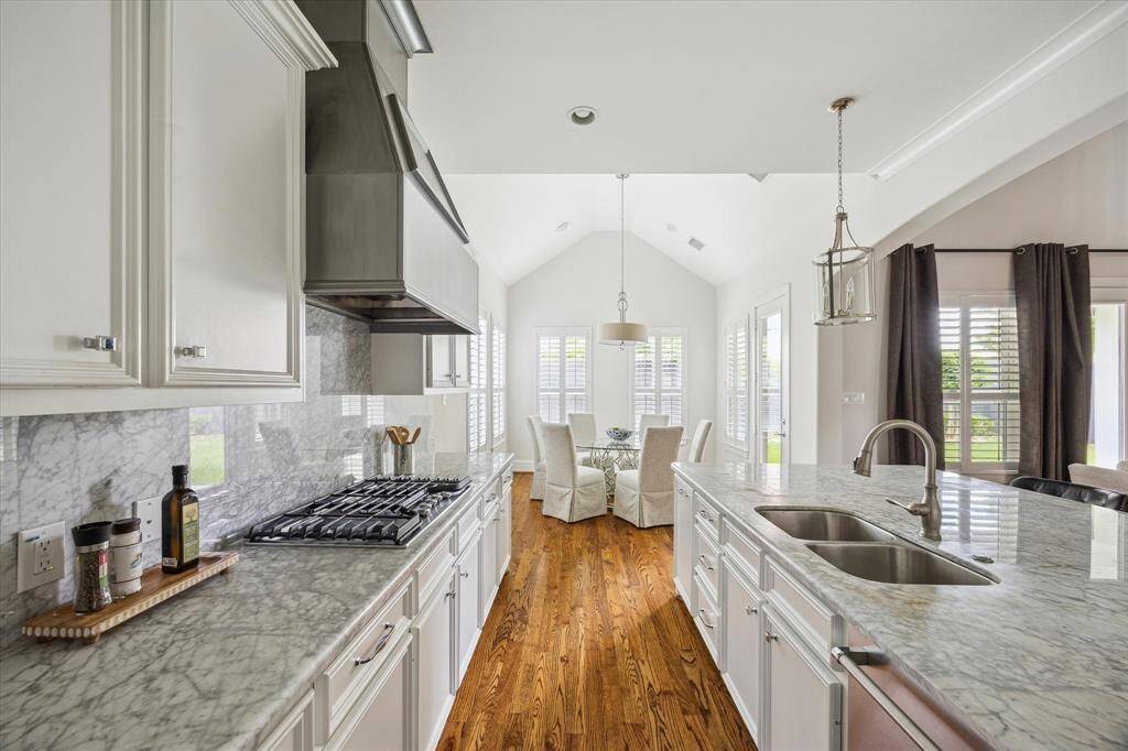 This kitchen showcases sleek marble countertops, a full marble backsplash, and premium stainless steel appliances, including a gas cooktop and vent hood.