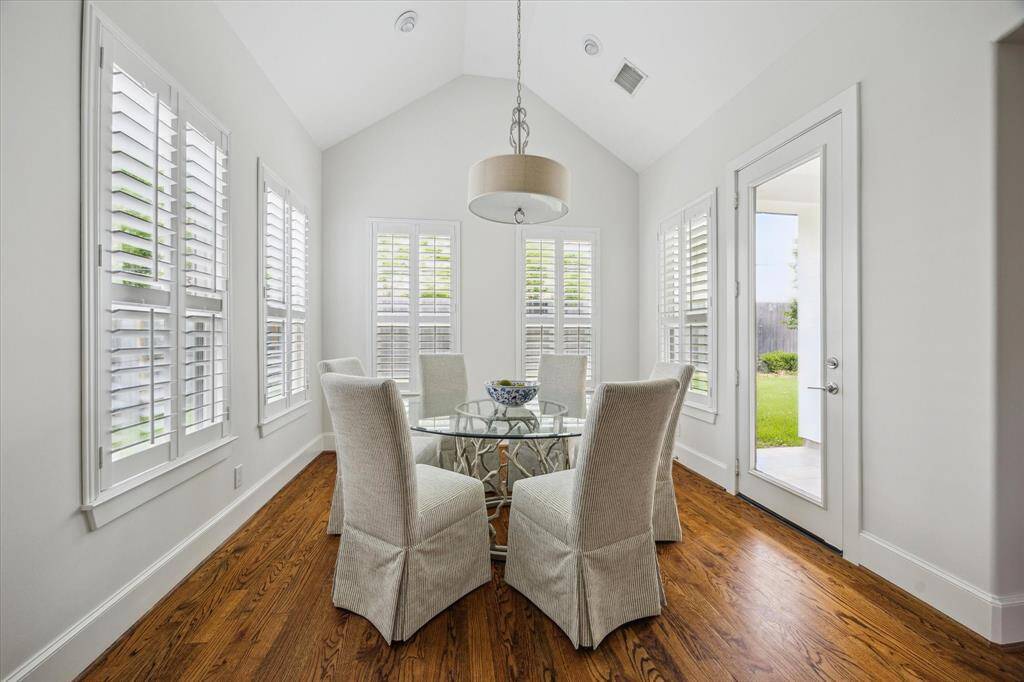 Bright breakfast room with a vaulted ceiling, surrounded by windows and a glass door offering views and access to the backyard.