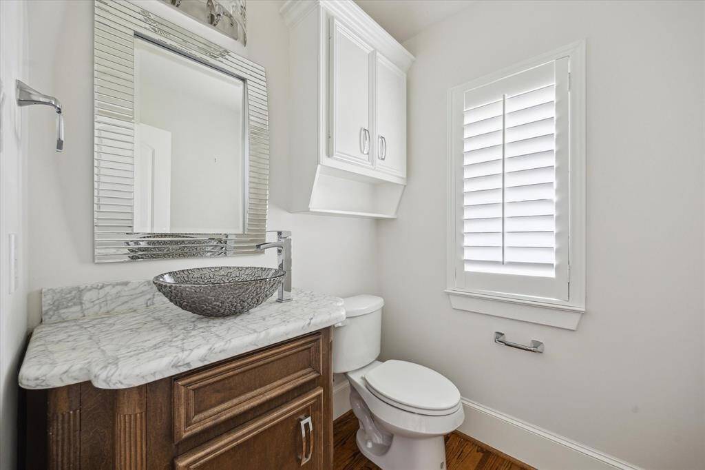 Stylish powder bathroom featuring a marble countertop, vessel sink, mirrored vanity, and window with built in shutters.