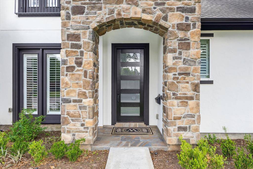 The front entry features a stone archway, modern glass-panel door, and a slate-tiled porch that adds texture and character to the clean exterior.