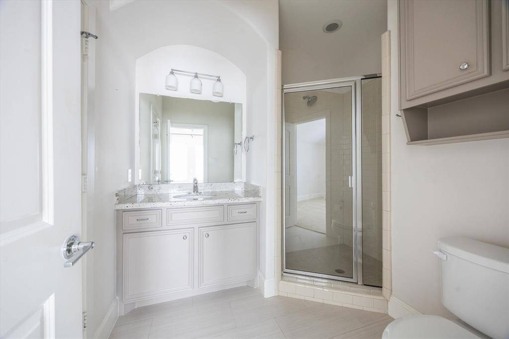 Secondary bathroom with a granite-topped vanity, large mirror, and a walk-in shower with glass enclosure.