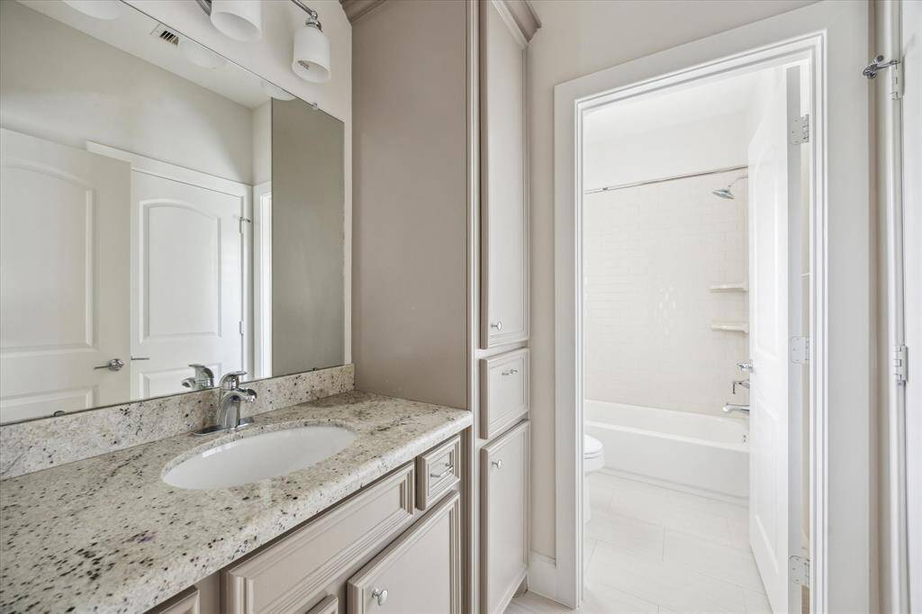 Secondary bathroom with granite countertops, ample cabinet storage, and a separate area with a shower/tub combo and subway tile surround.