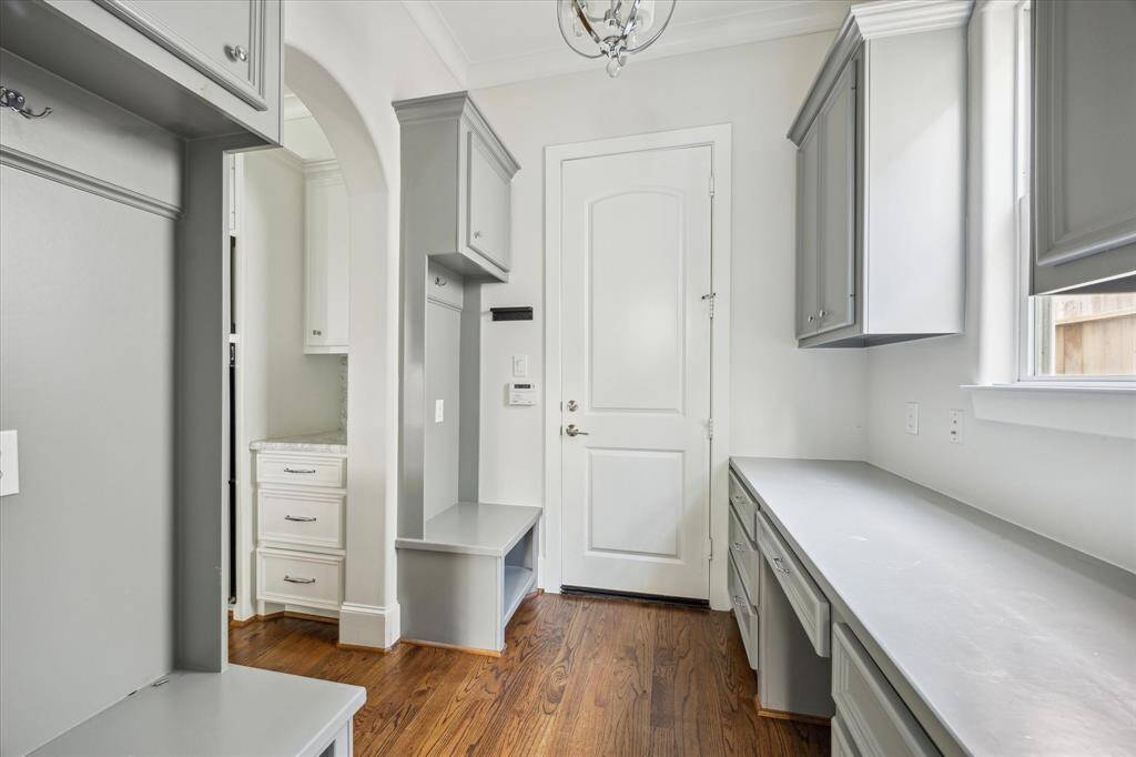 Functional mudroom with built-in bench seating, ample cabinet storage, and a long countertop workspace, all set on hardwood floors with backyard access.