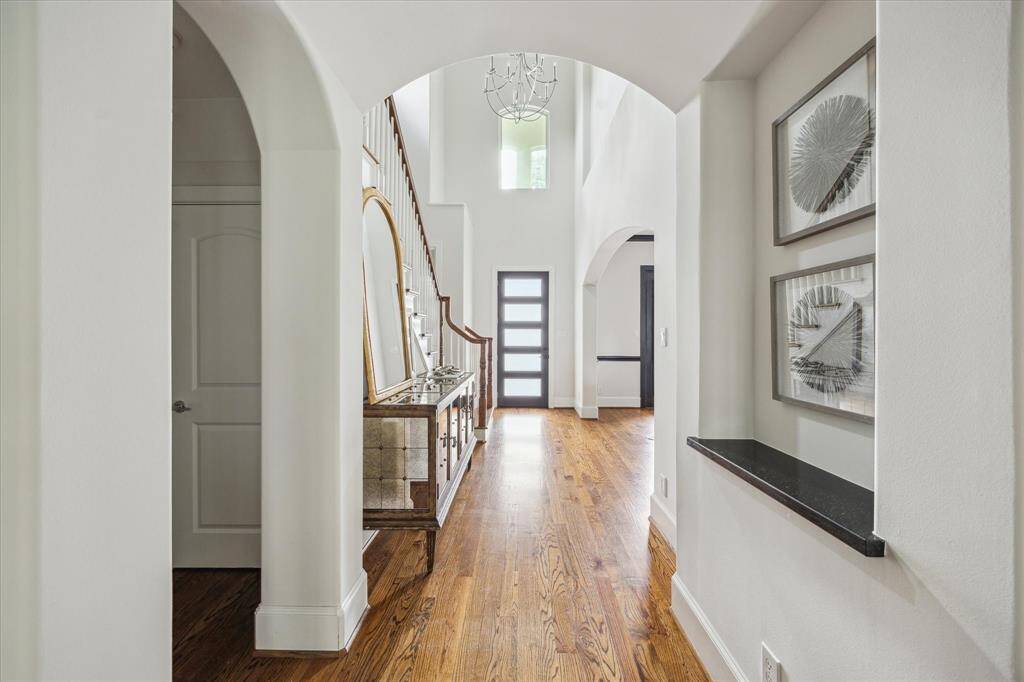 Bright entryway with soaring ceilings, arched openings, and warm hardwood floors leading to an open staircase.